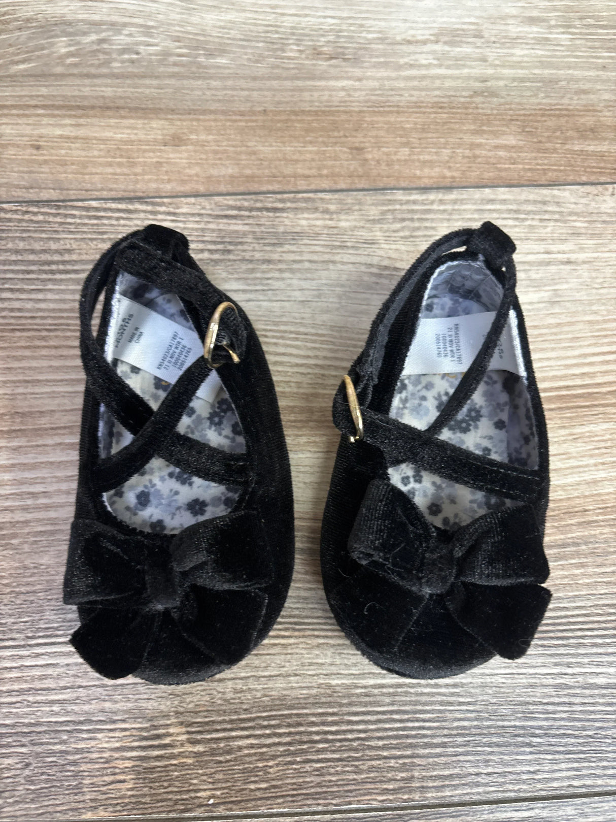 Black velvet baby girl shoes with bows and ankle straps on wooden floor