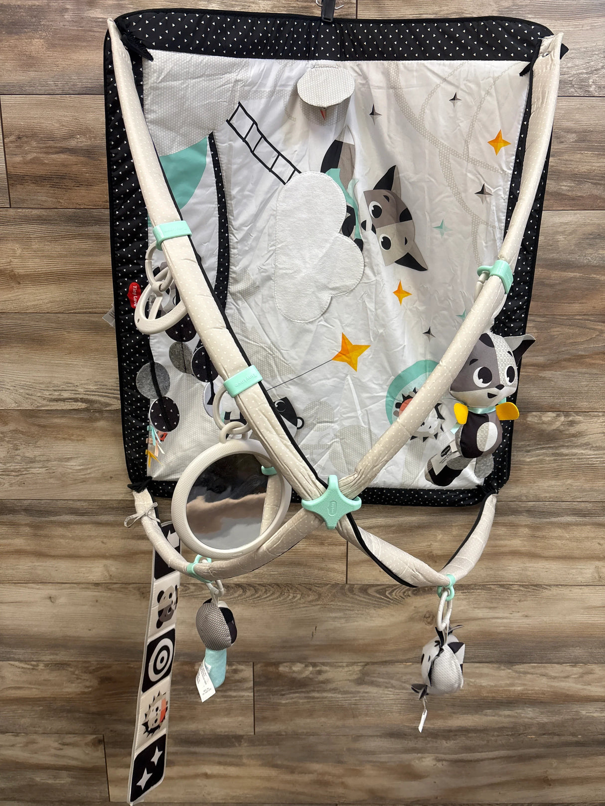 Top view of Tiny Love Gymini activity gym showcasing hanging toys, mirror, and black-and-white mat on wood floor