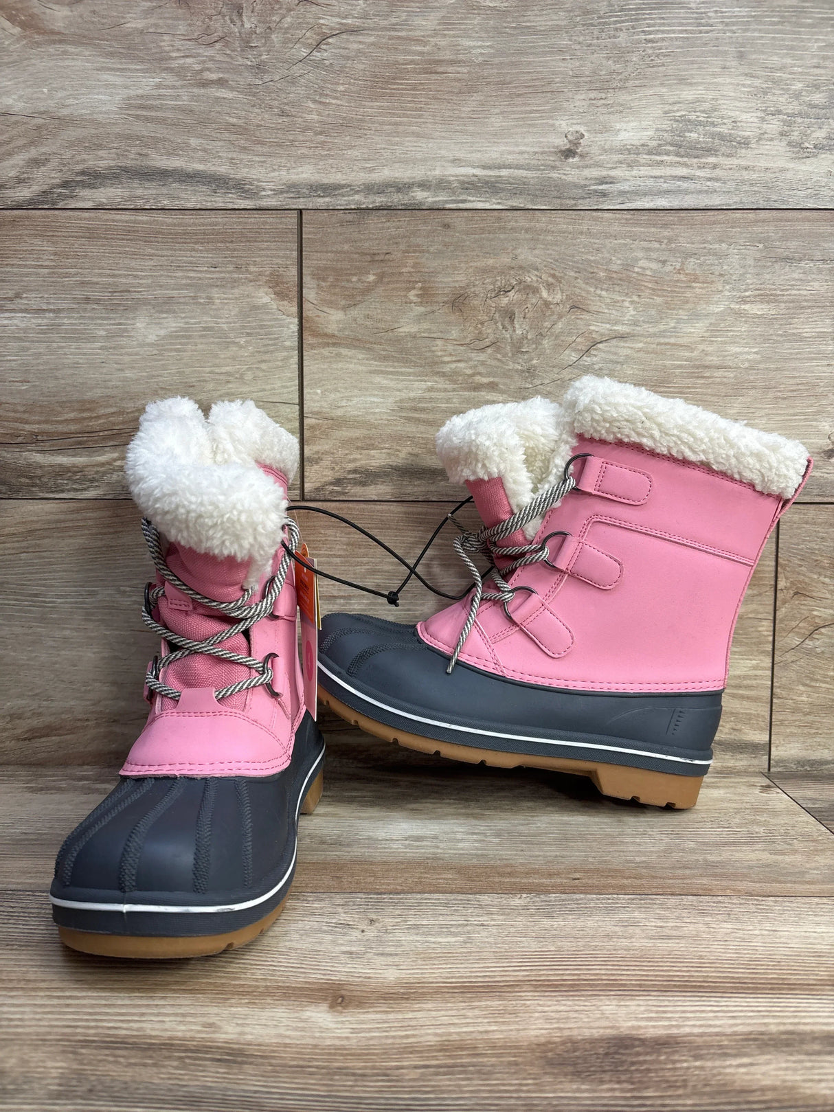 Pink kids winter snow boots with faux fur lining and rubber soles on wood floor