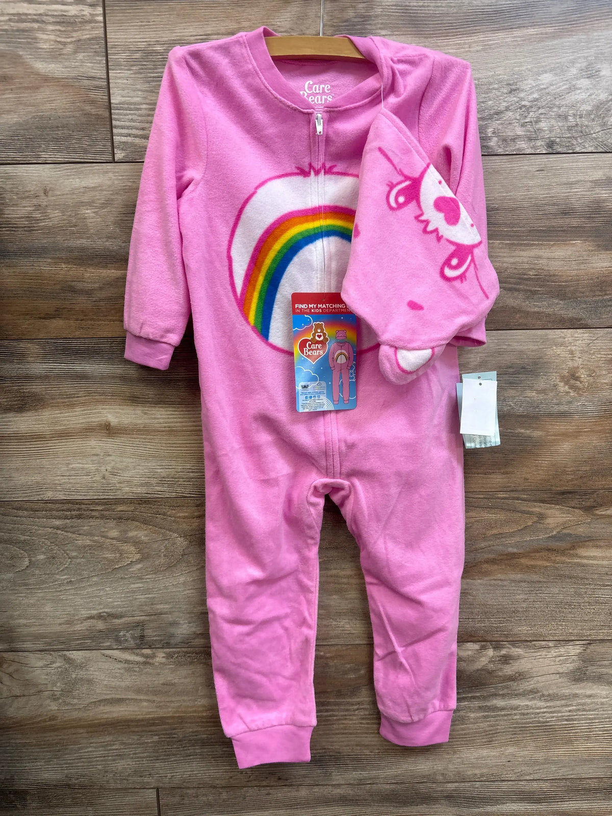Front view of pink Care Bears 2 piece hat and sleeper set in size 3T showcasing rainbow and unicorn graphics on a wood background