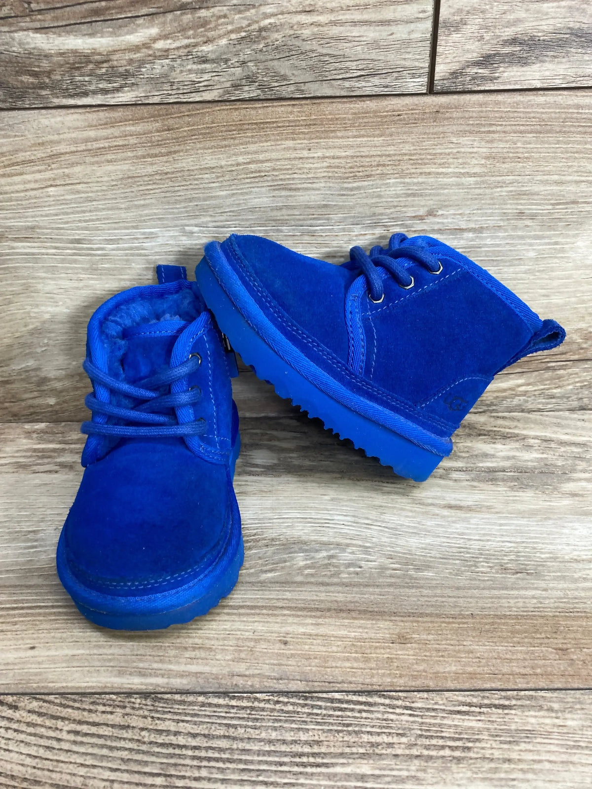 Bright blue suede toddler boots with laces on a rustic wooden floor