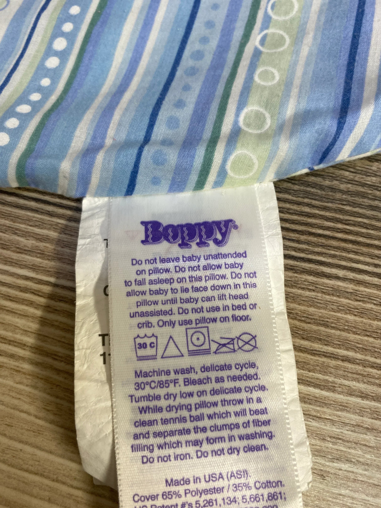 Boppy pillow care label with washing instructions and safety warnings on striped fabric background