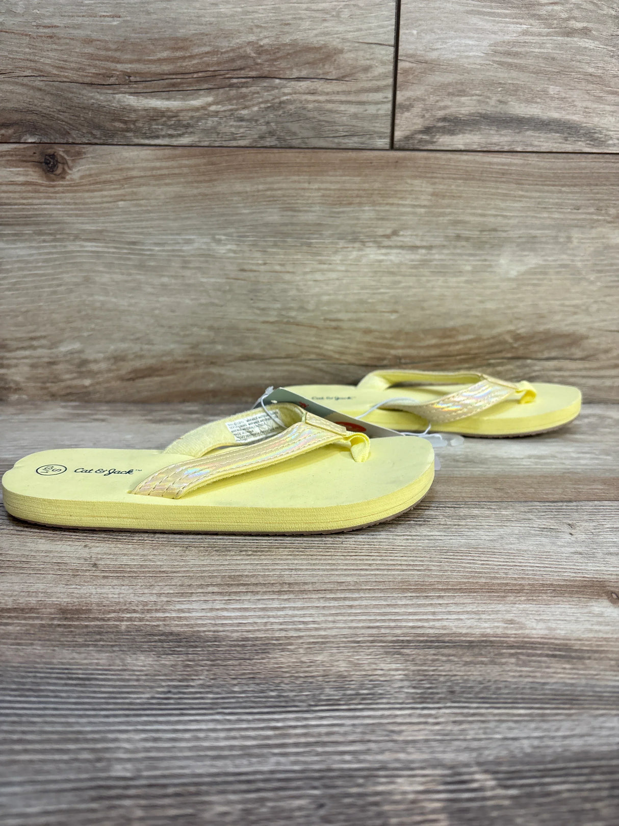 Yellow kids flip flops with iridescent straps on wood background, Cat & Jack brand