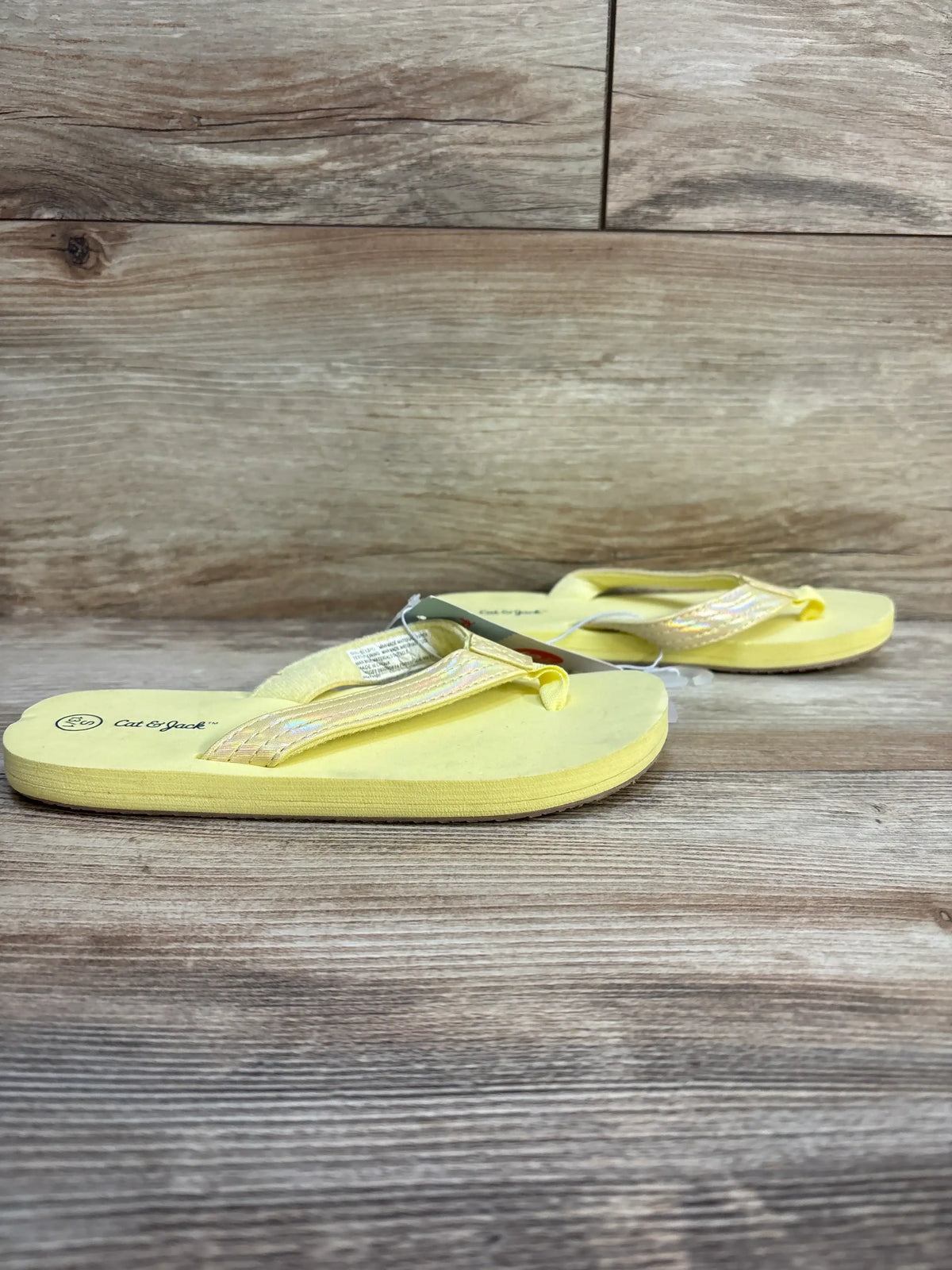 Top view of Cat & Jack Ava toddler flip-flop pair in yellow showcasing iridescent straps on a wooden floor