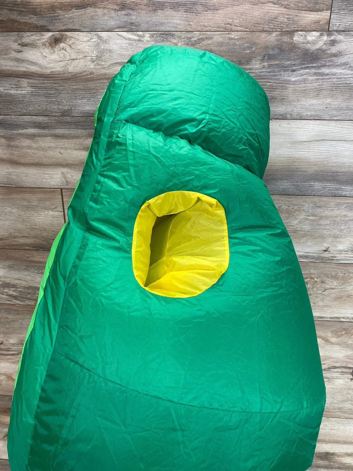 Front view of green avocado inflatable costume showcasing yellow pit opening with wood plank background