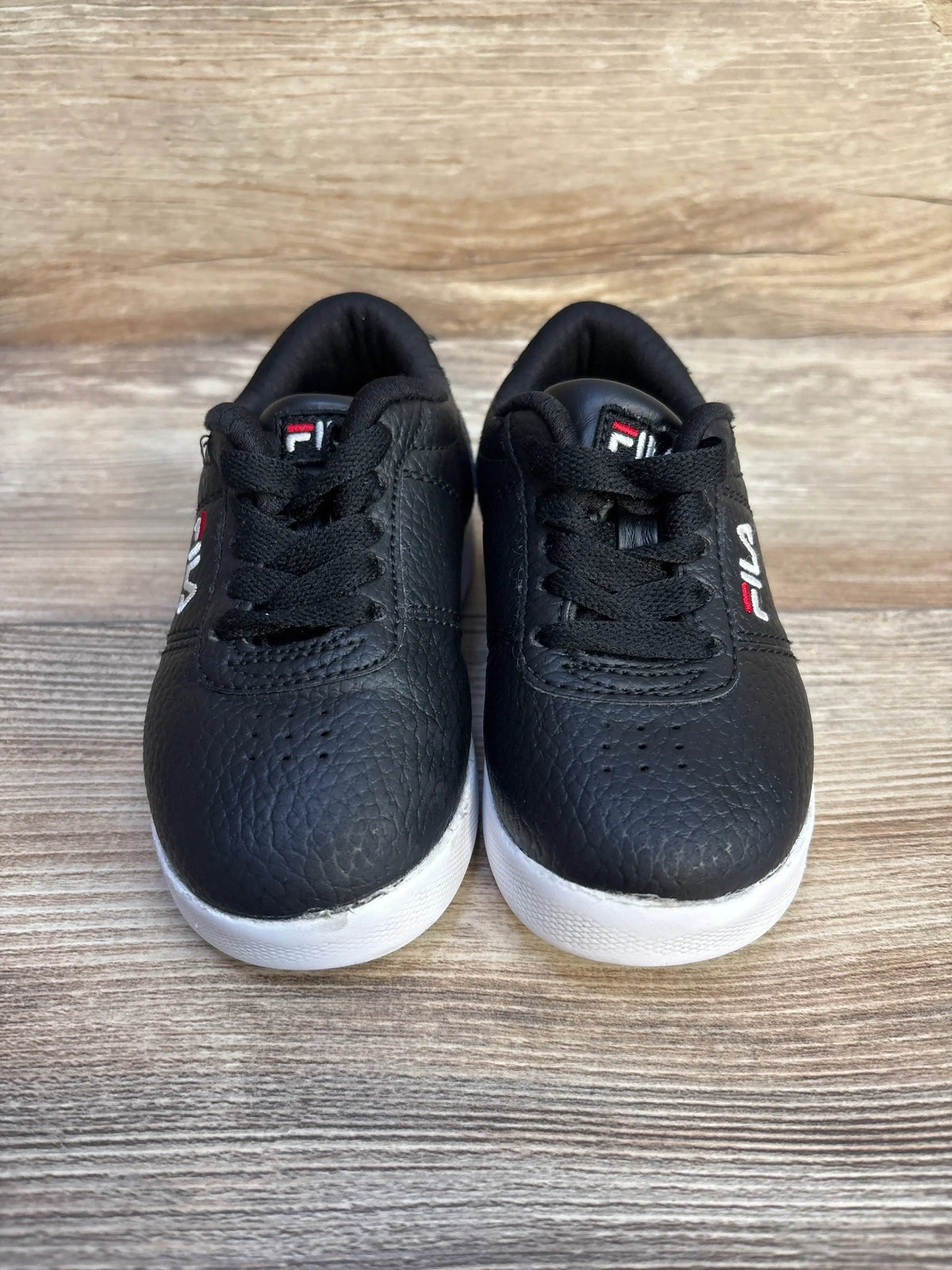 Pair of black FILA leather sneakers with white soles on wooden surface