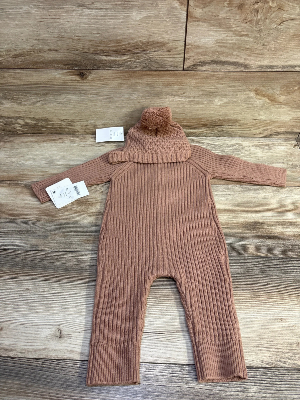 Flat lay of Grayson Mini 2pc knit button coverall and pom-pom hat showcasing ribbed knit texture on wood background, brown, size 3-6 months
