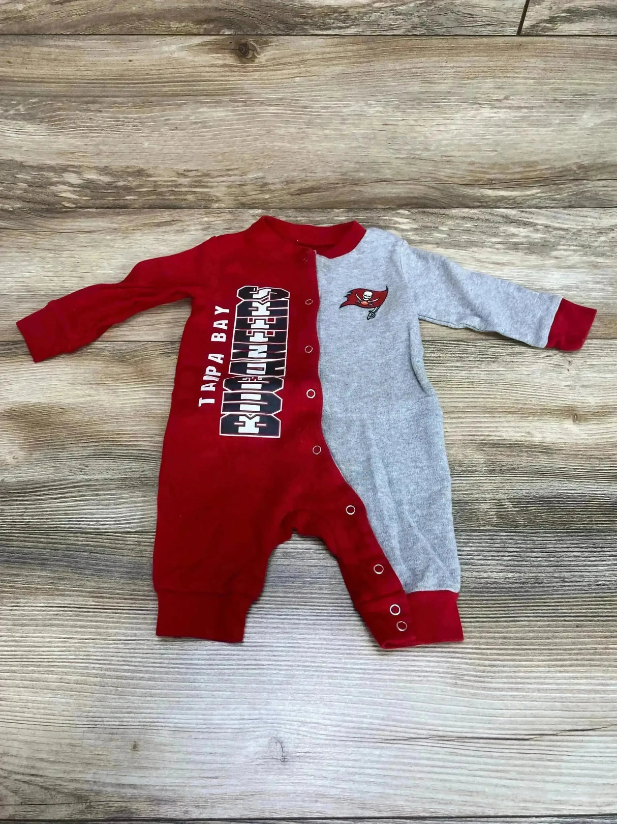 Flat lay of red and gray Buccaneers baby coverall 0-3 months showing front snaps, team logo and print on wood background