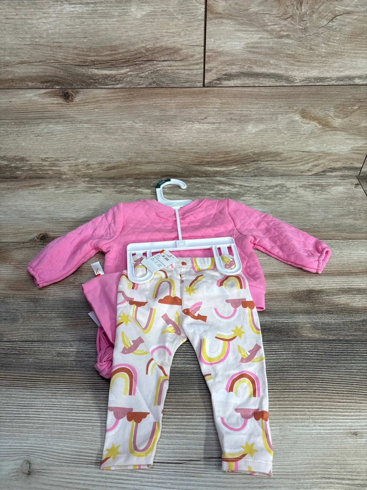 Pink quilted baby sweater with white leggings featuring colorful rainbow and star patterns on wooden floor
