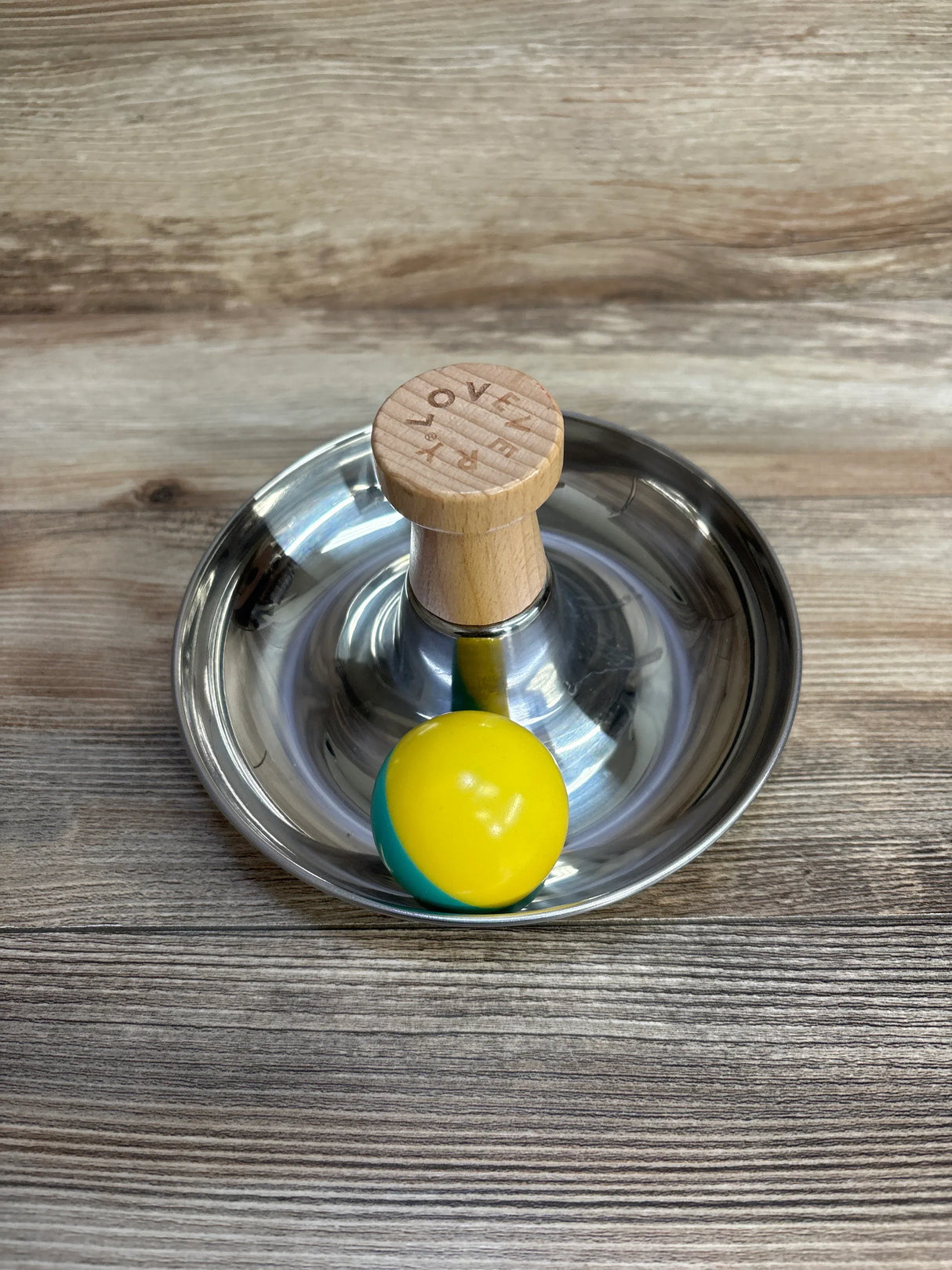 Wooden handle metal tamper in steel dish with yellow green ball on wood surface