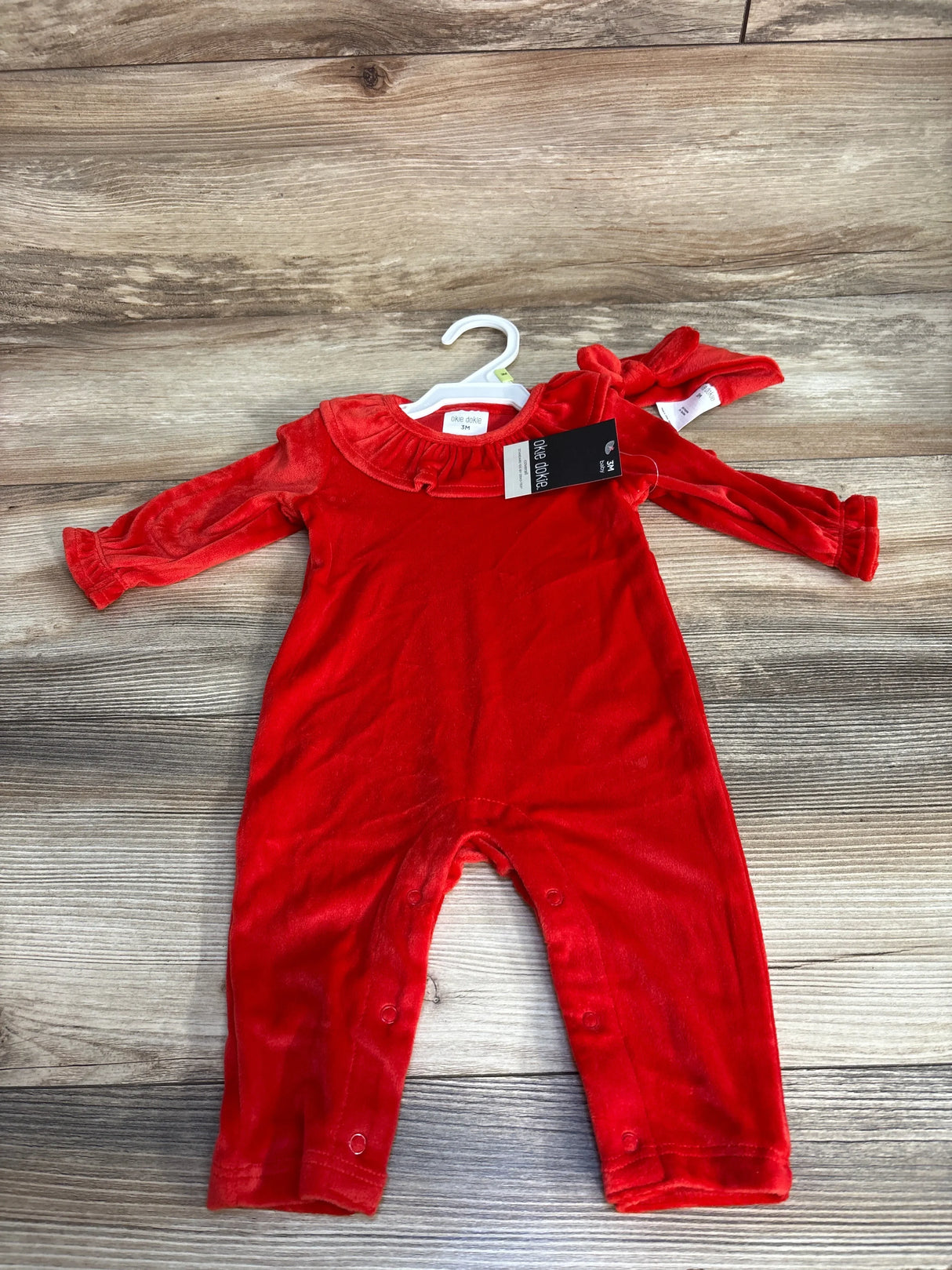 Red velvet baby romper with ruffle collar and snaps, displayed on wood floor