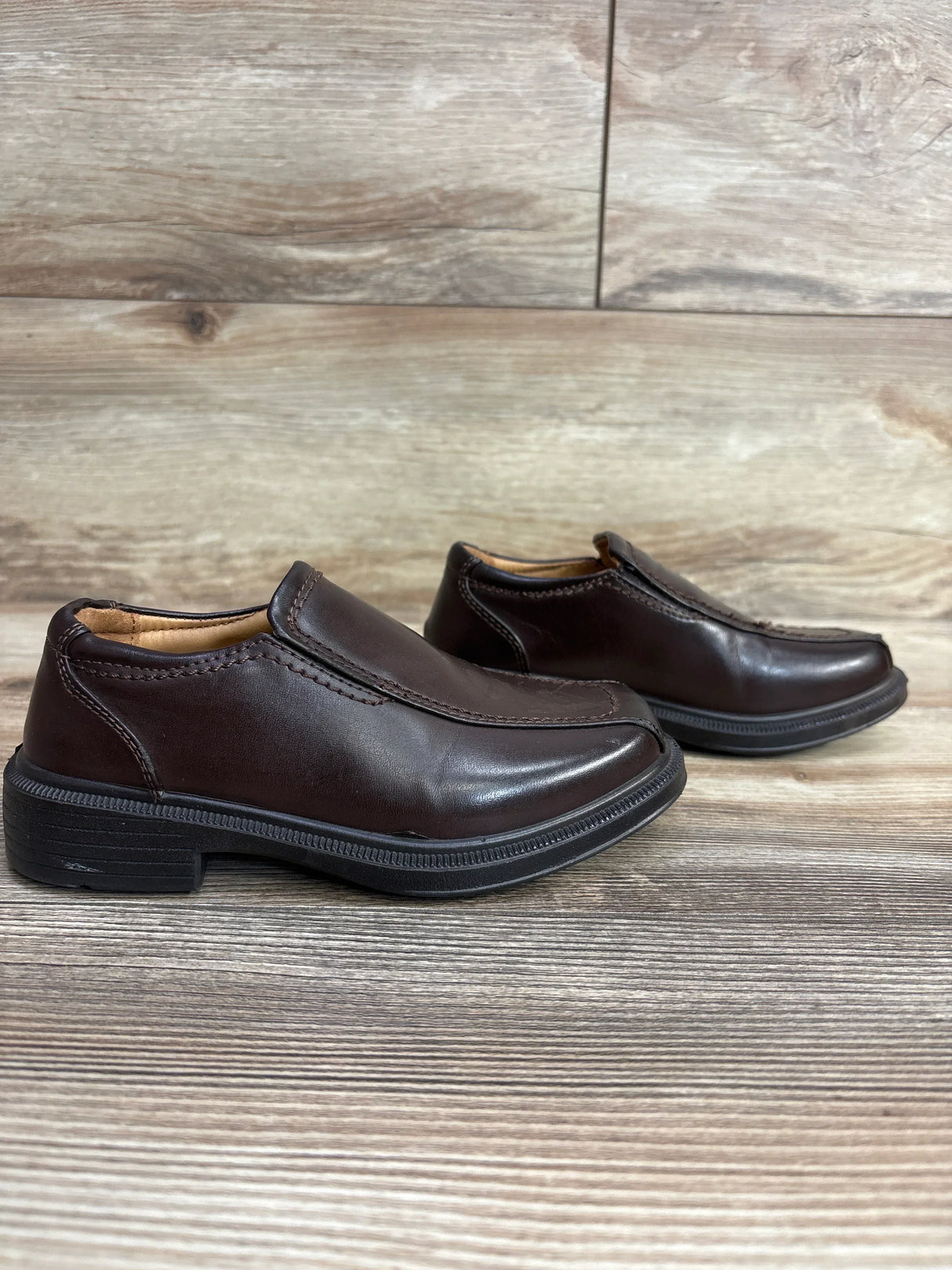 Pair of dark brown leather slip-on shoes with black soles on wood floor background