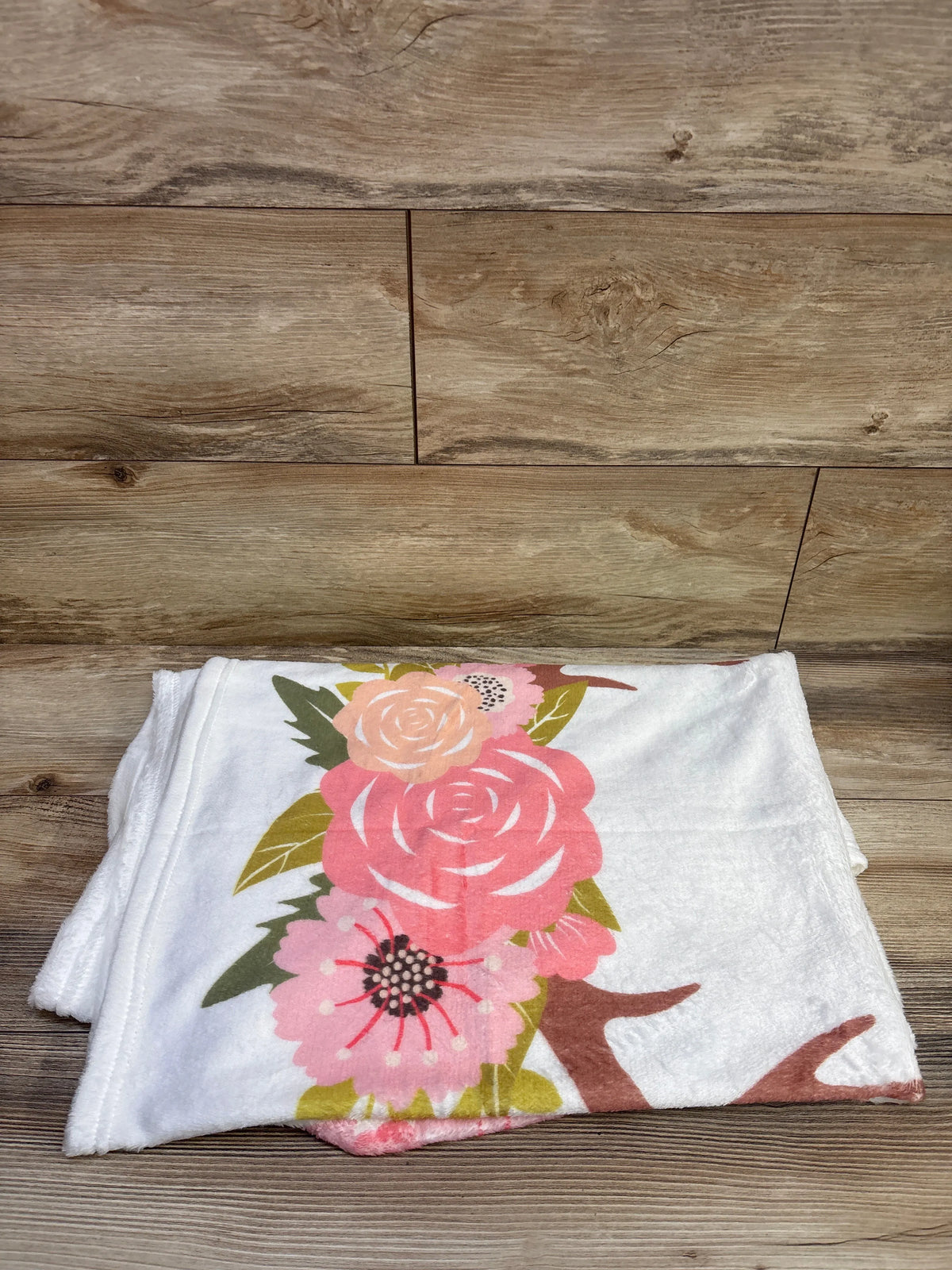 Folded white milestone blanket showcasing a colorful floral print on a wood floor