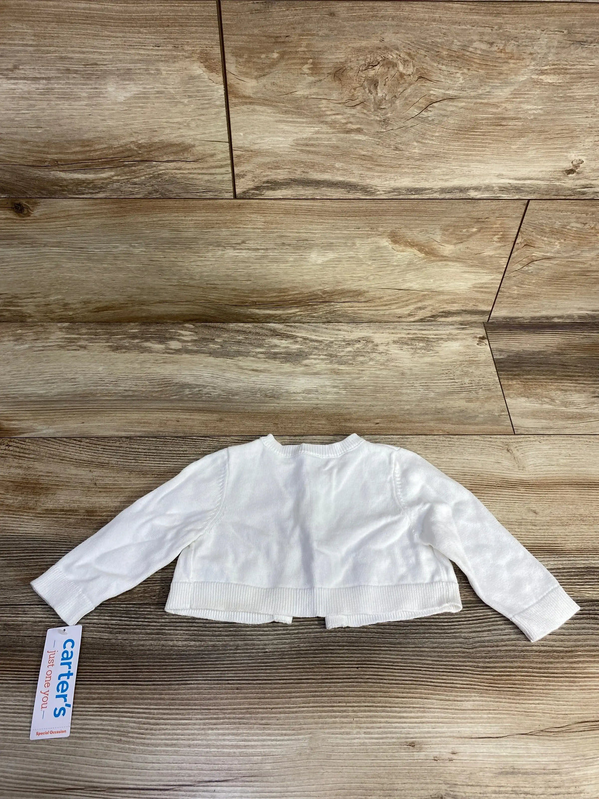 White long-sleeve baby cardigan sweater from Carter's with tag on wood background