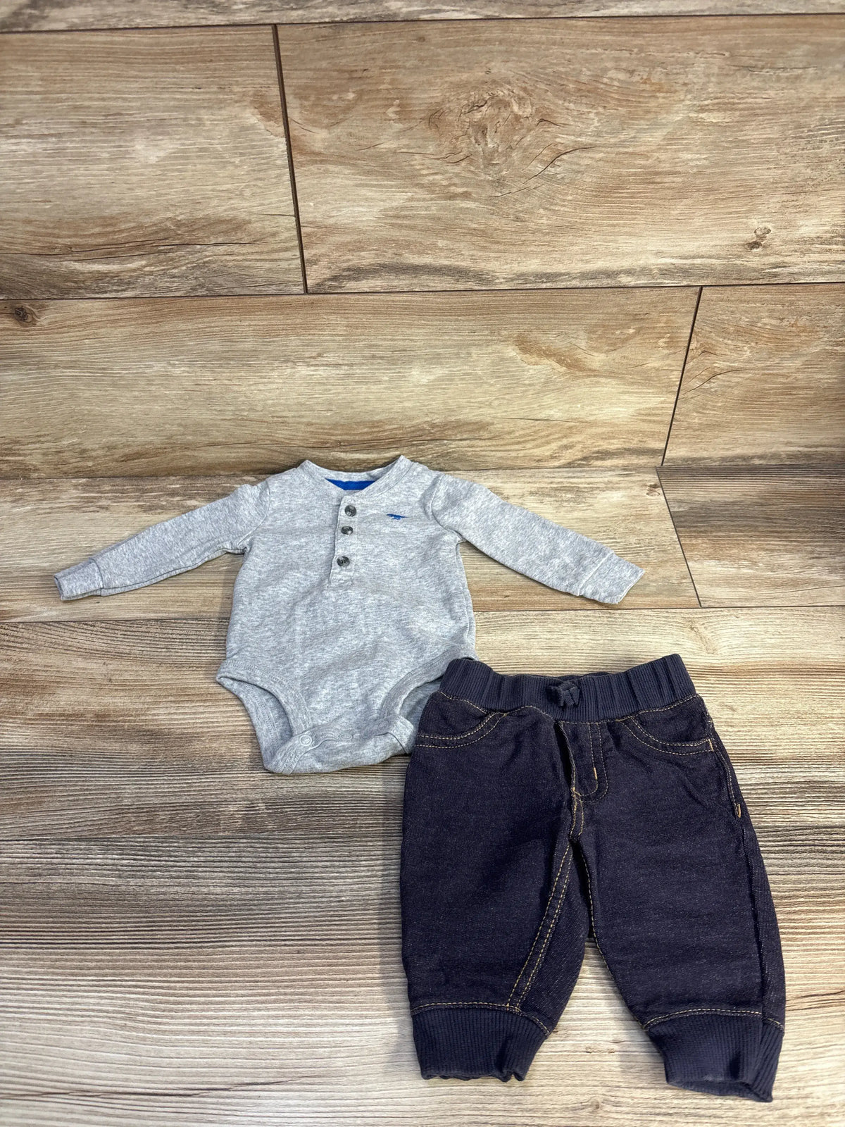 Top-down view of Carter’s baby henley bodysuit and jeggings set, gray ribbed bodysuit and dark jeggings on wood flooring