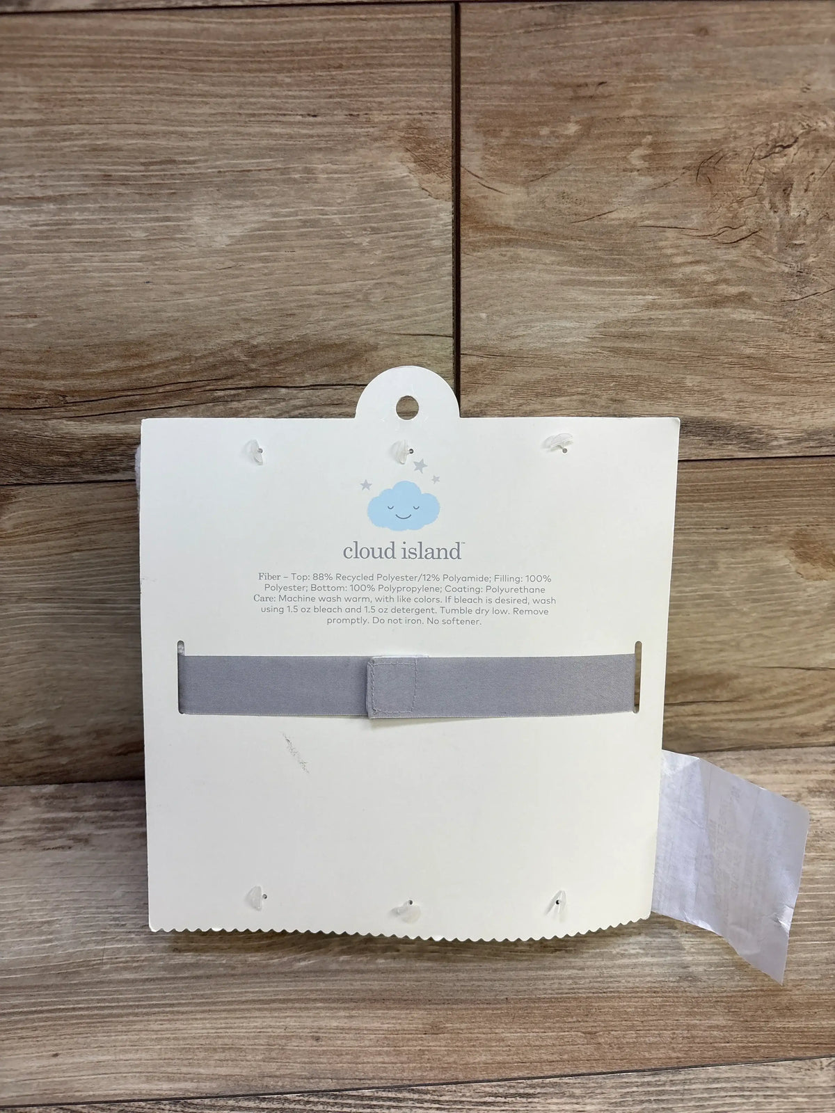 Back of Cloud Island changing pad liners showing blue cloud logo, gray fabric strap and care text on white card over wood background