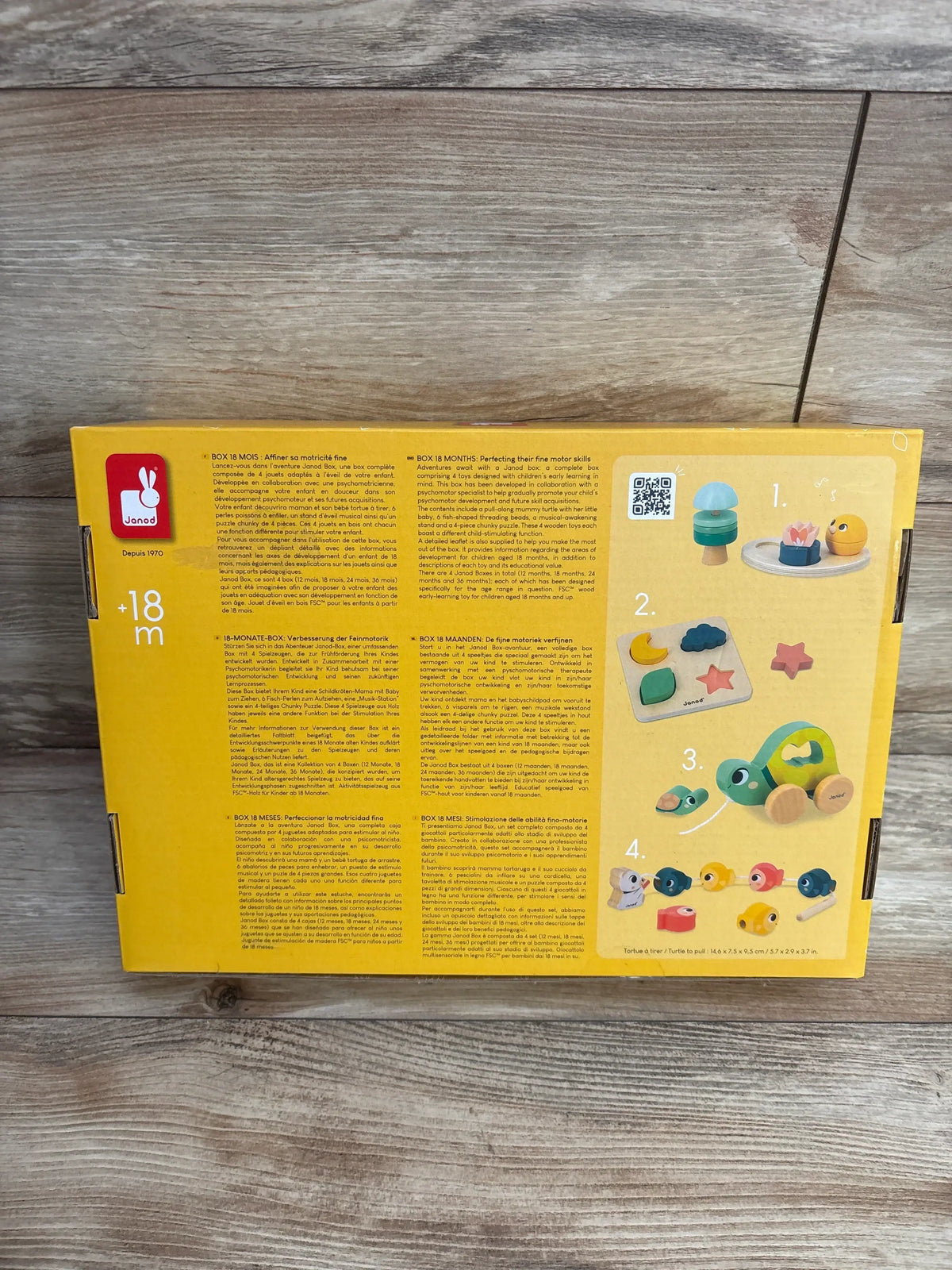 Back view of NEW Janod Baby Play Box showcasing turtle, bead threading, musical toys, and chunky puzzle activities on a wood surface