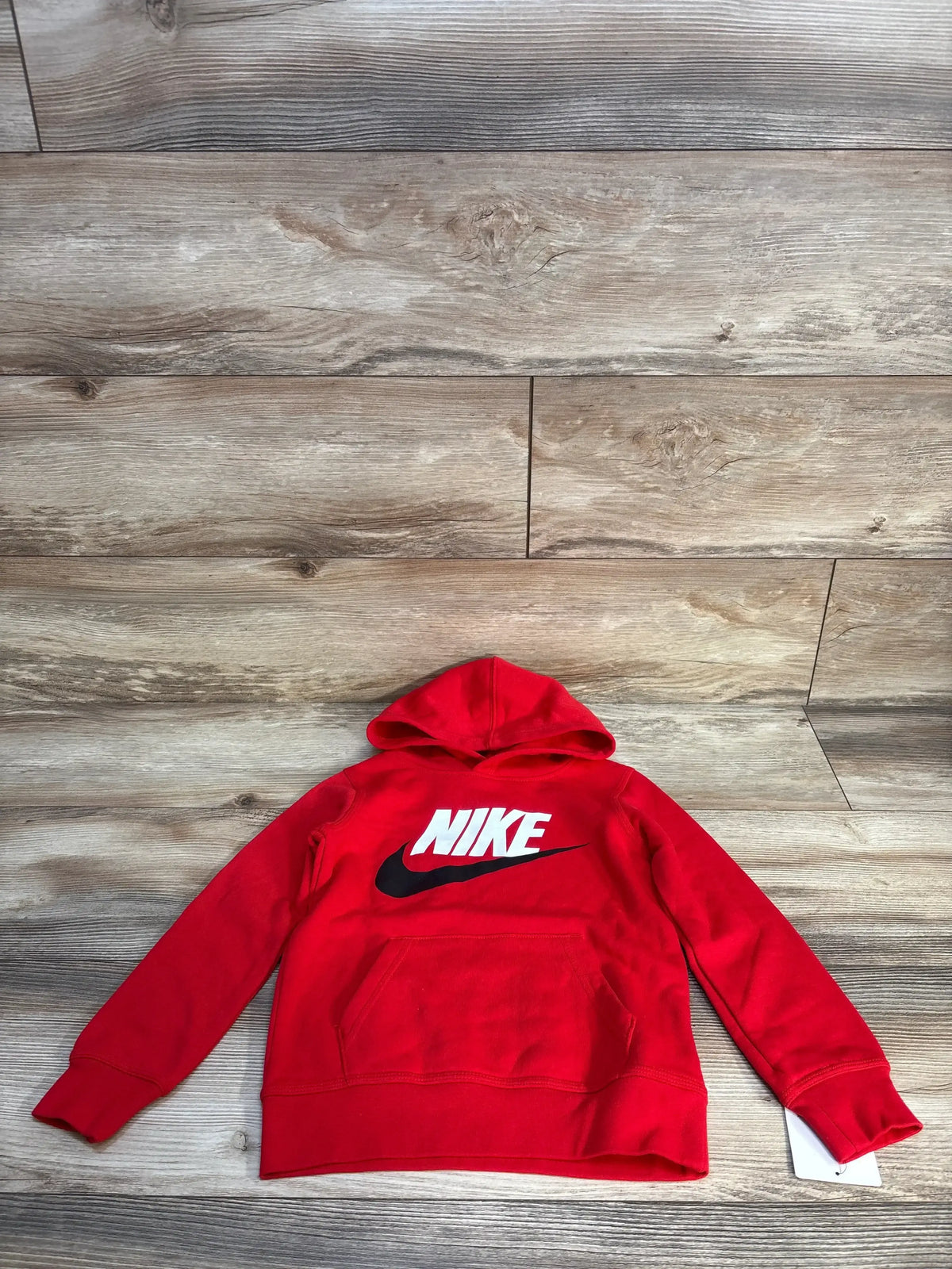 Red Nike kids hooded sweatshirt with front pocket laid flat on wooden background