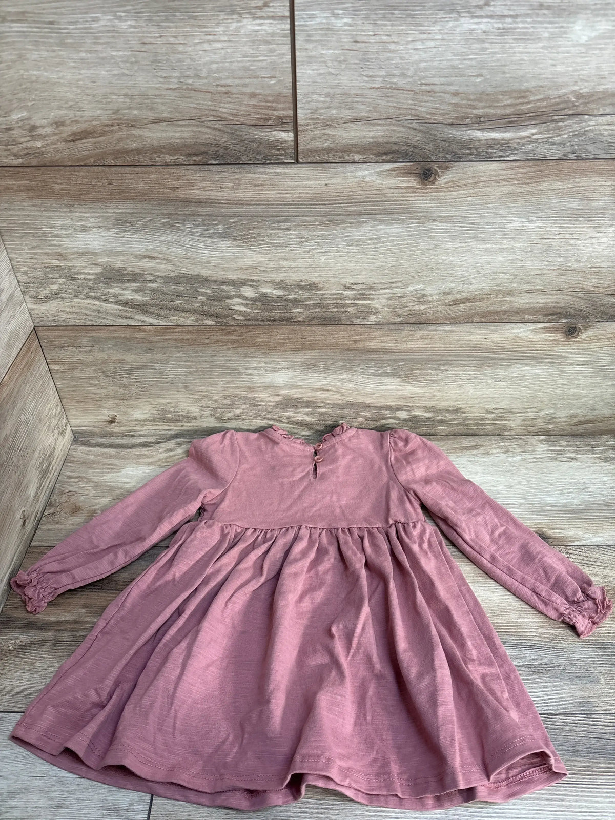 Long-sleeve dusty rose baby dress with ruffled collar and button back on wood background