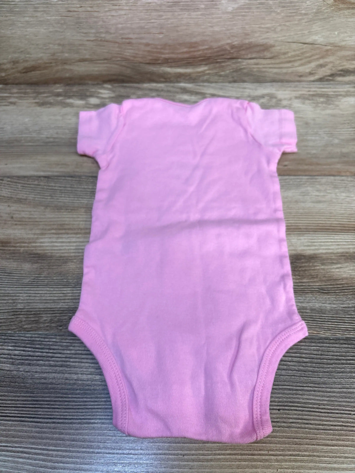 Top down view of Carter’s pink 12 month baby bodysuit showing short sleeves and leg openings on a wood surface