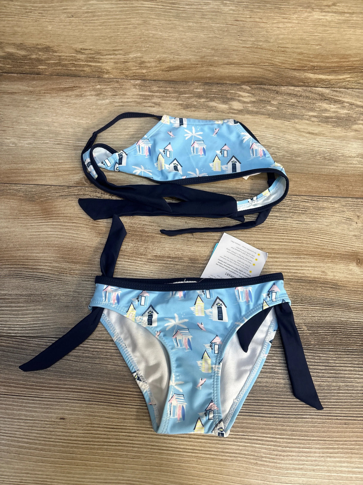Light blue girls bikini set with beach hut print and navy tie straps on wood background