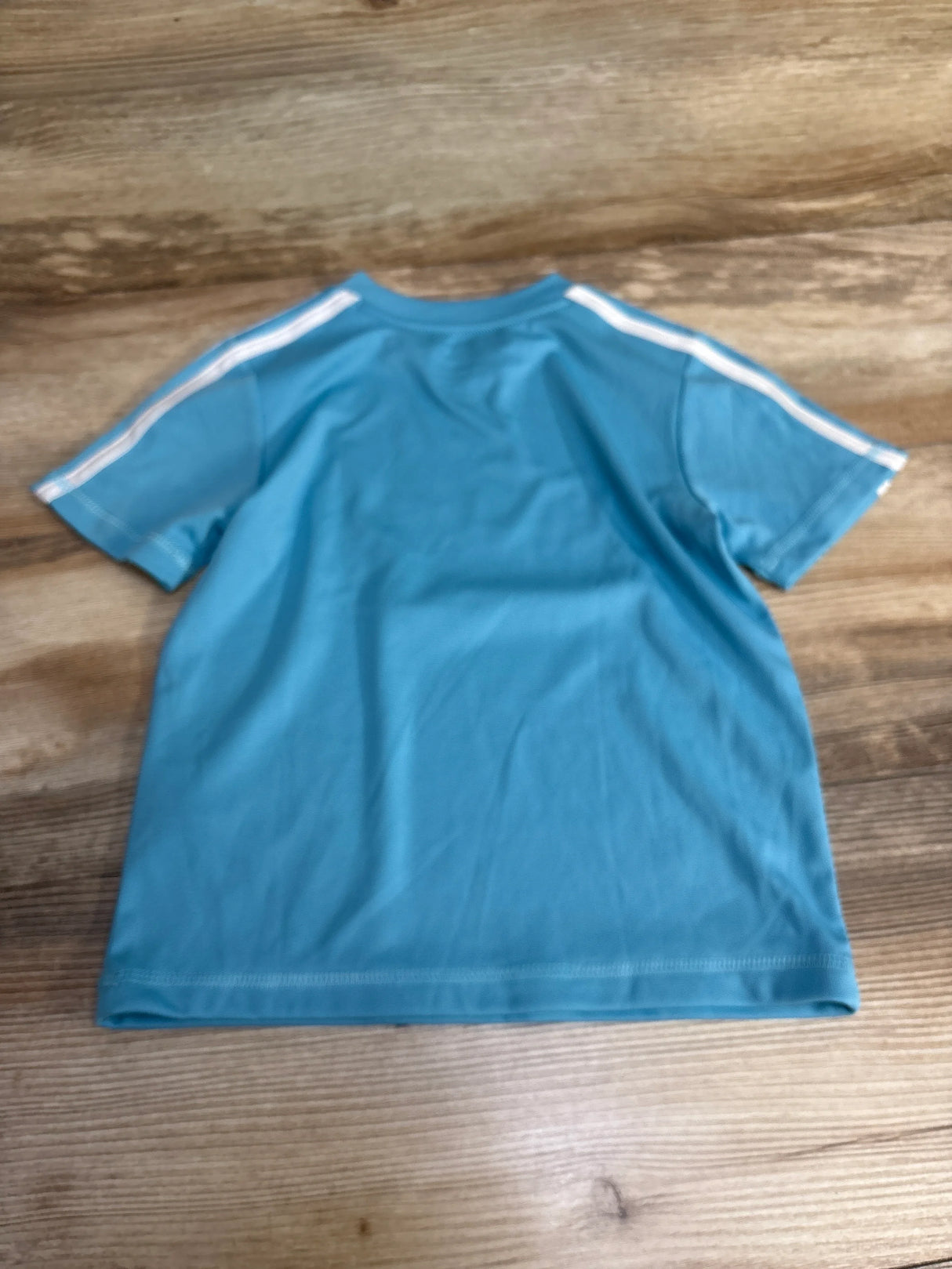 Blue short sleeve t-shirt with white shoulder stripes on wooden background