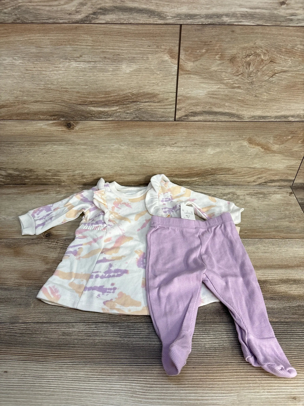 Pastel tie-dye baby dress with lavender footed pants on wood background