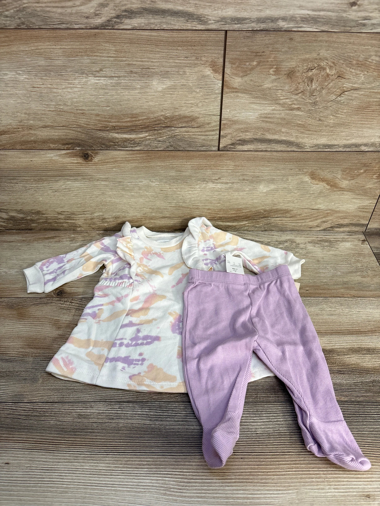 Pastel tie-dye baby dress with lavender footed pants on wood background