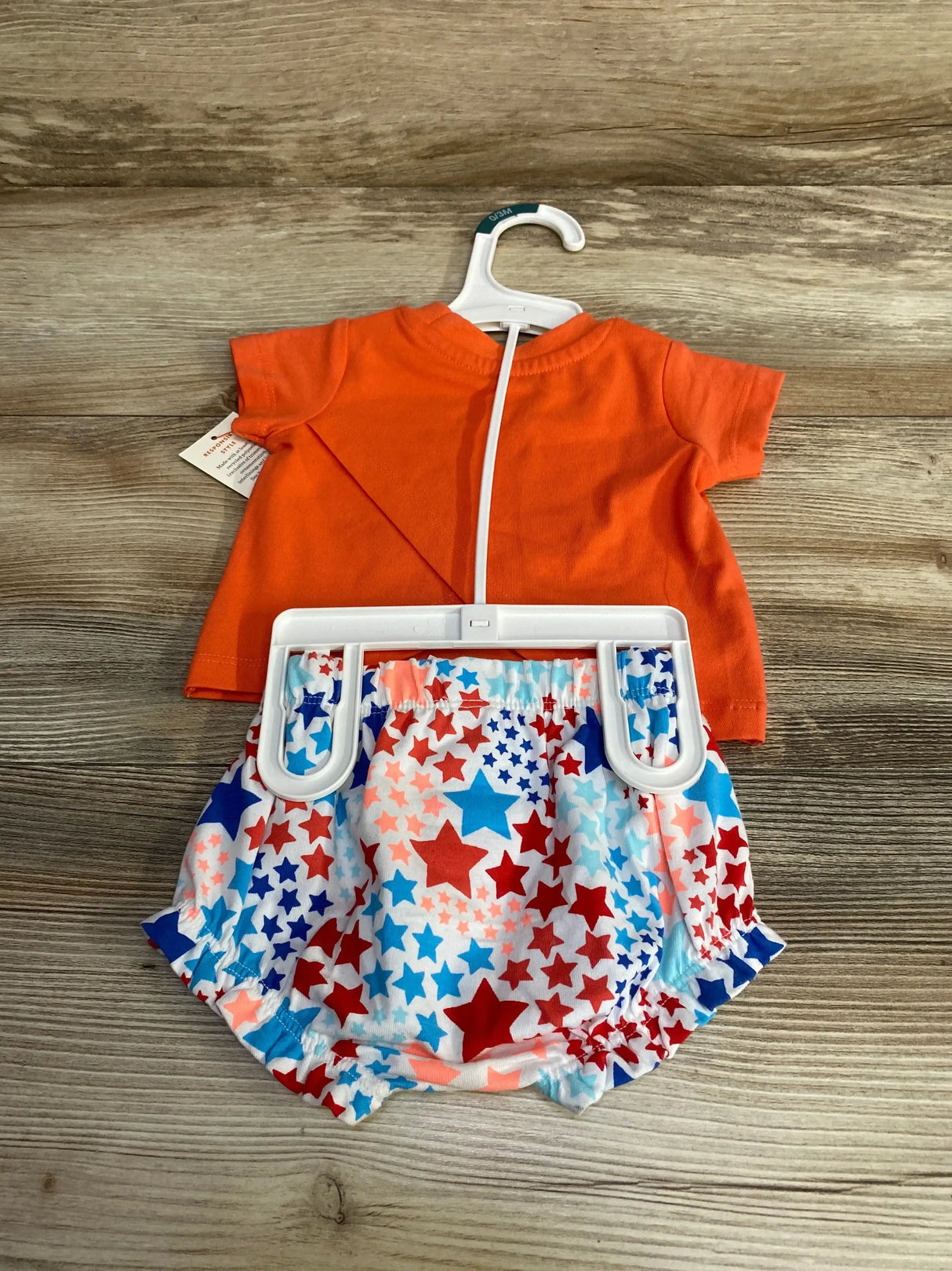 Flat lay of newborn orange tee and matching star-print shorts on a white hanger on wood background
