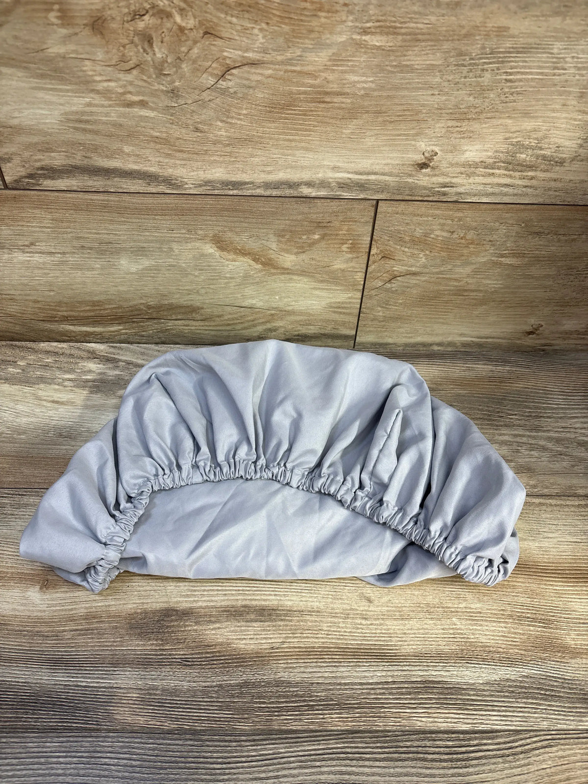 Top view of a grey Parent’s Choice fitted bassinet sheet showcasing gathered elastic edges on a wood-look floor