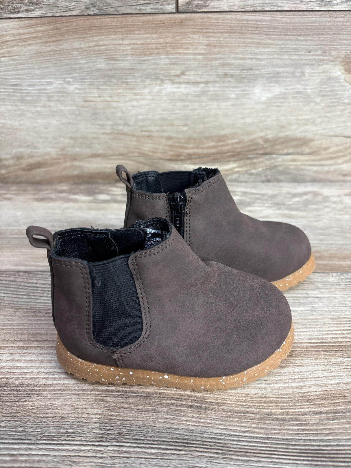 Pair of toddler brown suede ankle boots with black elastic sides and speckled rubber soles on wooden surface