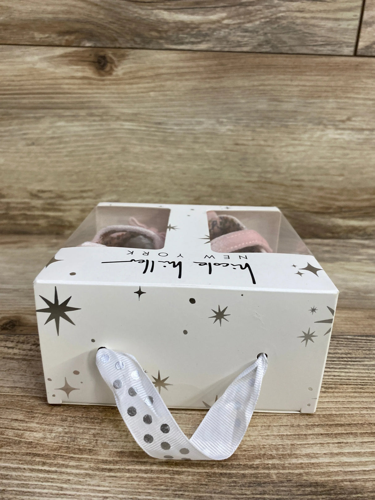Gift box with pink baby shoes, polka dot ribbon handle, and star pattern on wood surface