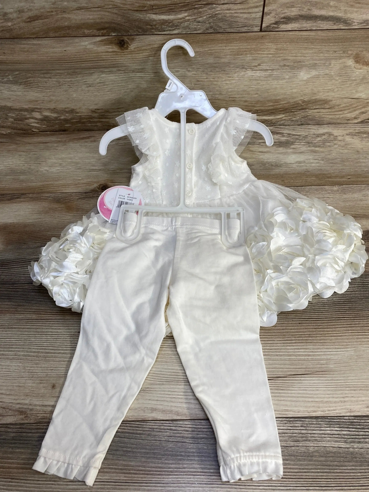 Front view of ivory rosette dress and matching leggings showing layered rosette skirt and tulle cap sleeves on wood floor