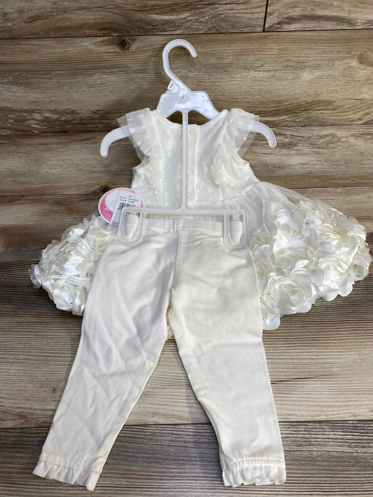 Front view of ivory rosette dress and matching leggings showing layered rosette skirt and tulle cap sleeves on wood floor