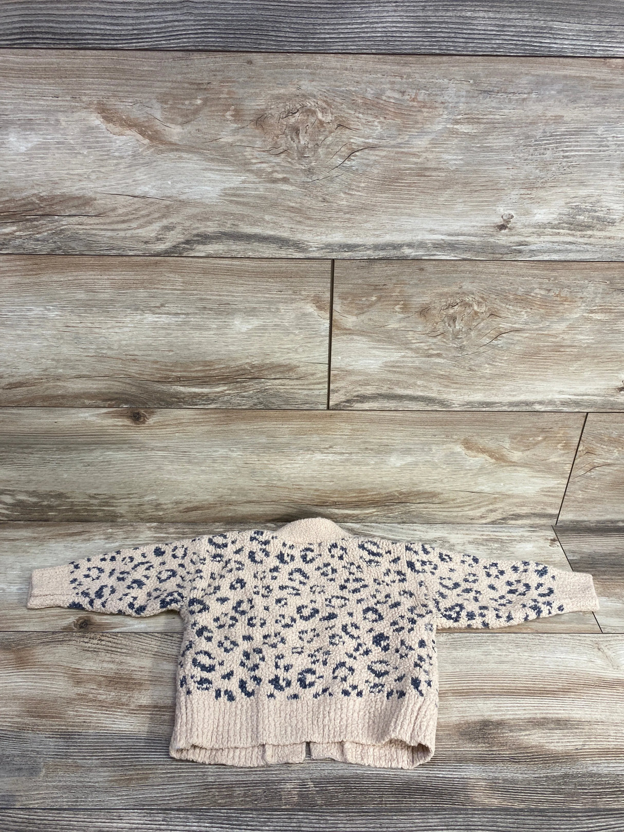 beige and black leopard print fuzzy sweater laid flat on wooden floor