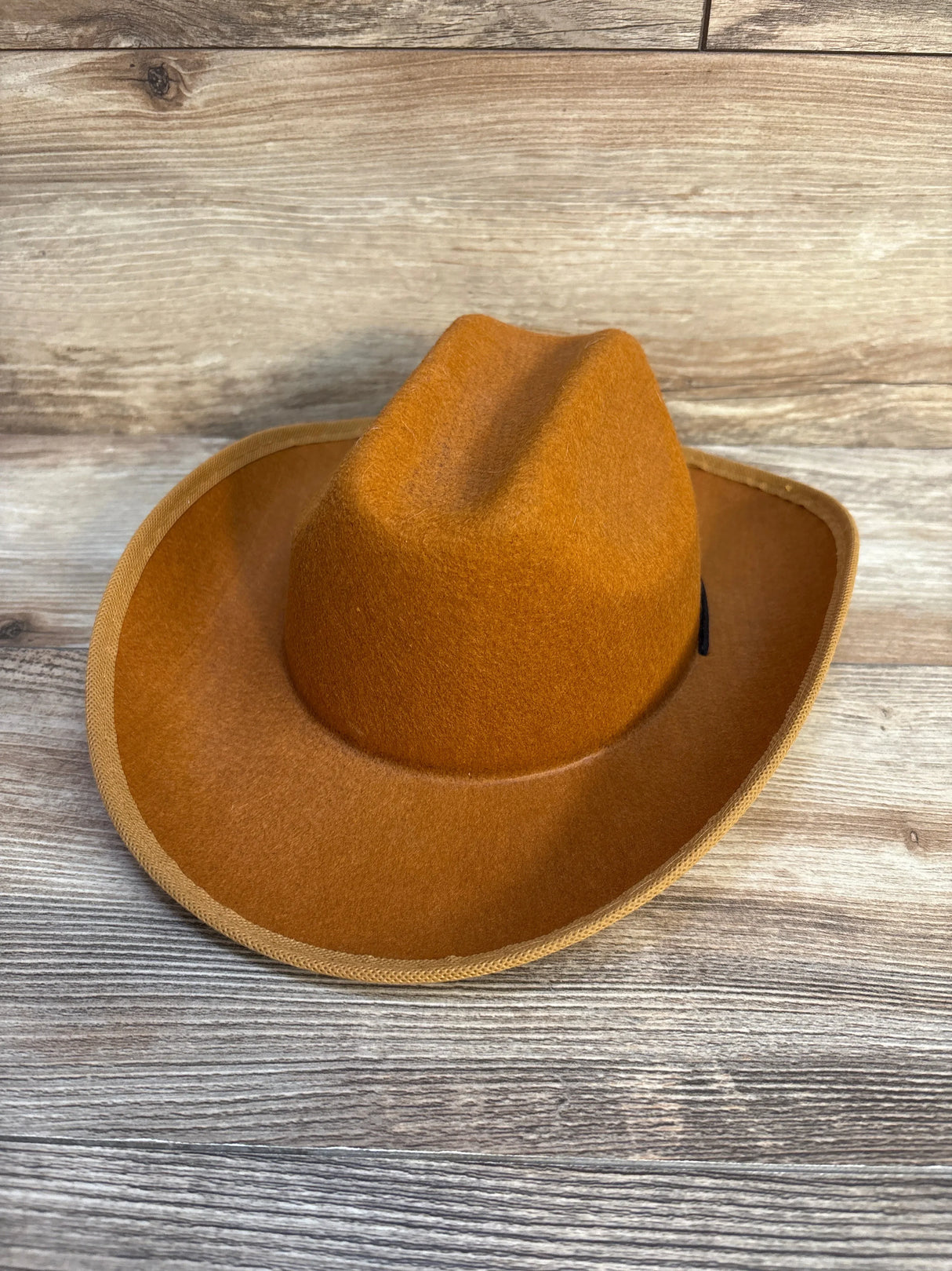 Brown felt cowboy hat for kids, perfect for playtime or costumes, set on wooden background