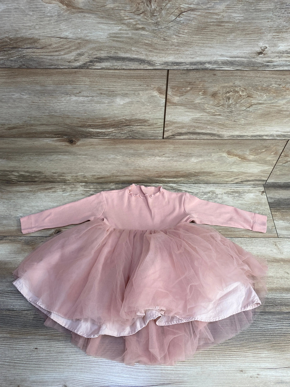 Flat lay of Amica long sleeve lace tulle baby dress in pink showing lace bodice and layered tulle skirt on wooden floor