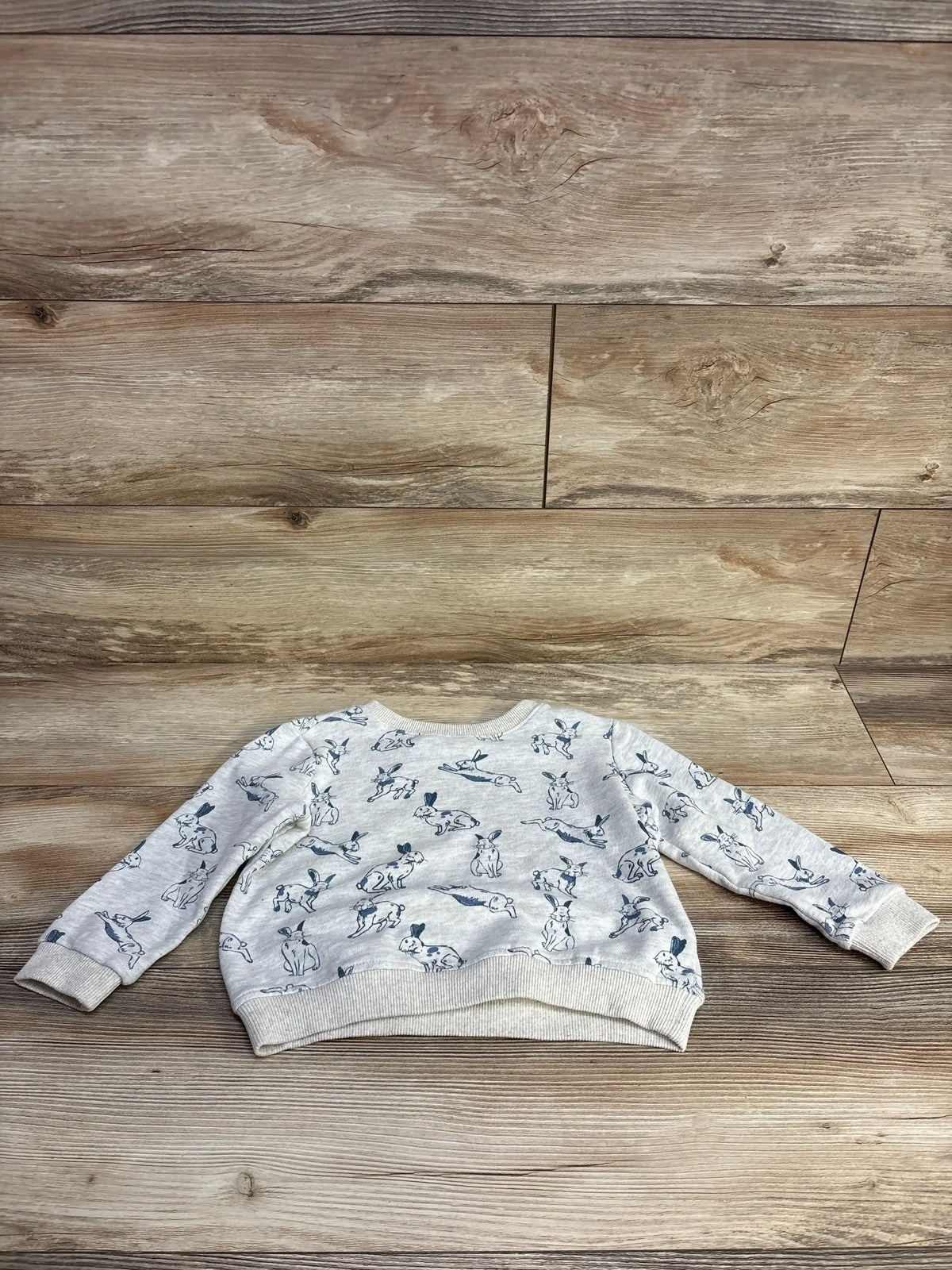 Flat lay back of grey toddler pullover sweatshirt showing navy bunny print and ribbed cuffs on wood floor