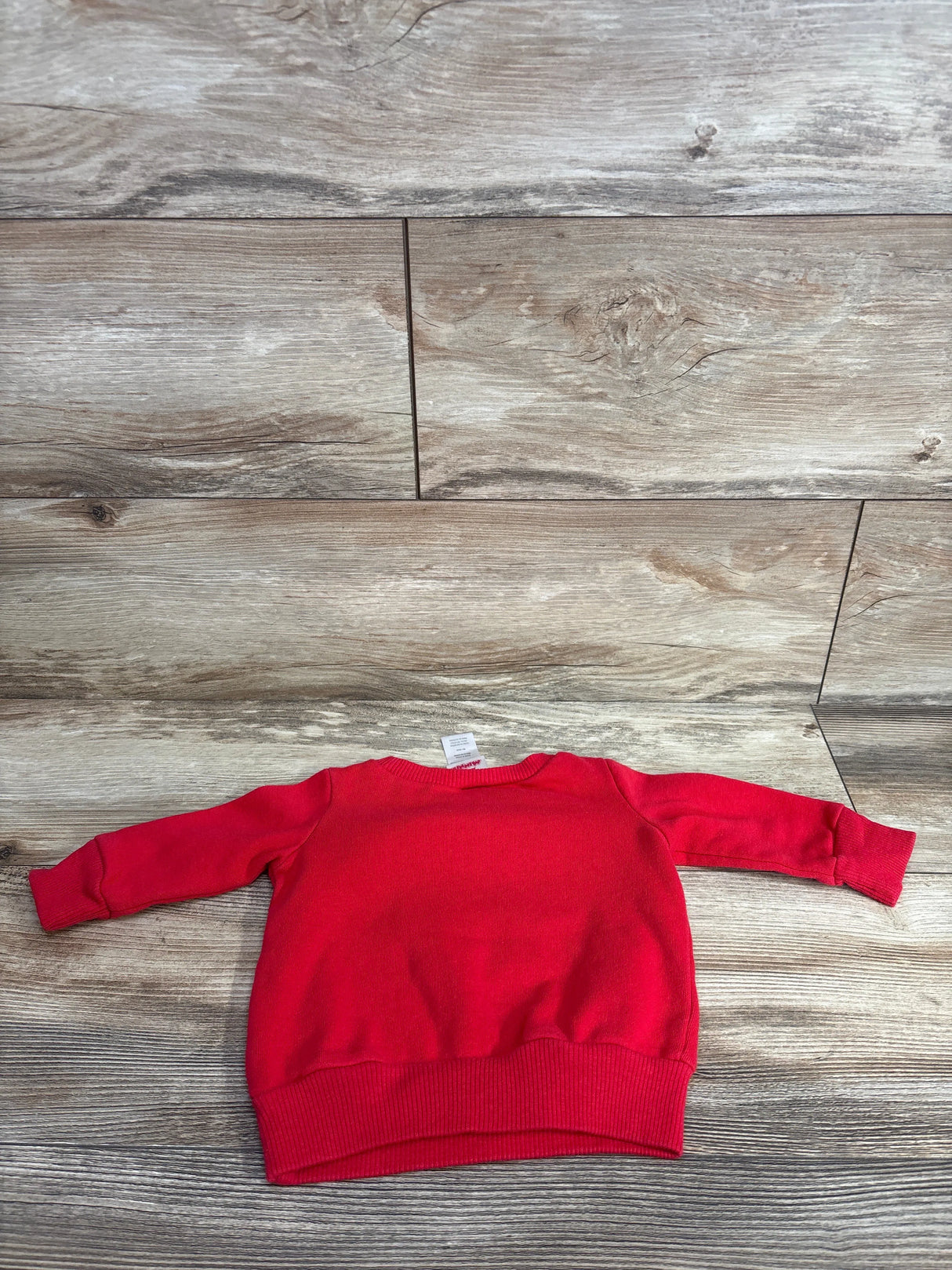 Red long-sleeve toddler sweater laid flat on wood floor background children's clothing