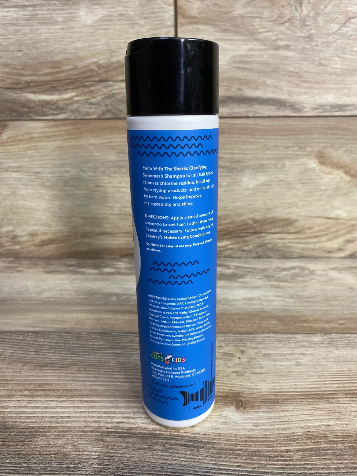 Rear view of Sharkey's Swimmer's Clarifying Shampoo (10 oz) showing blue label with directions and ingredient list on wood background