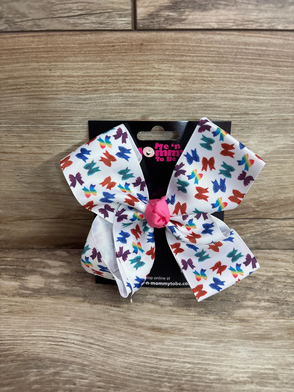 Front view of large printed hair bow showcasing multicolored butterfly pattern and pink center knot on black card and wood background