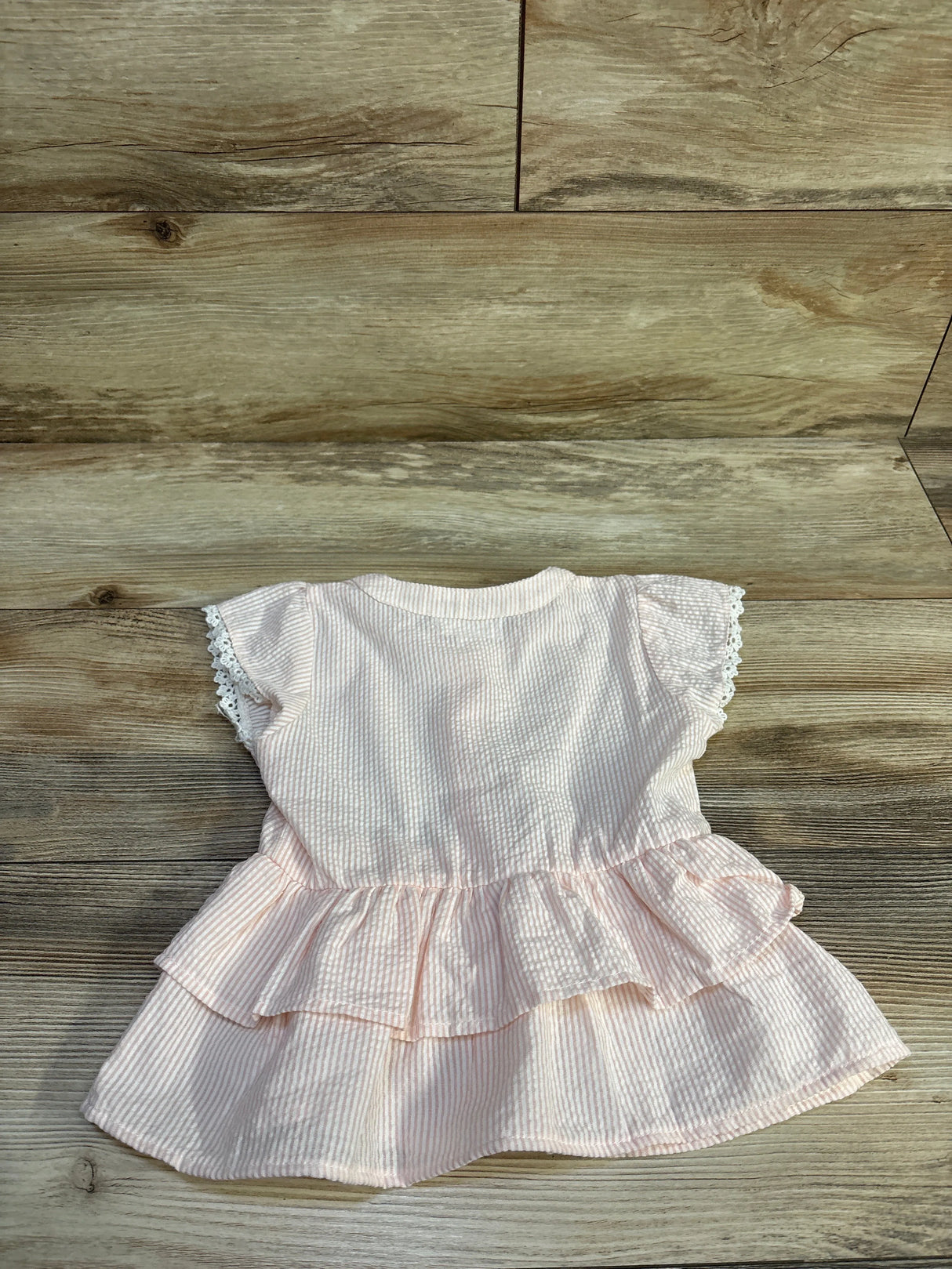Back view of Koala Kids pink striped seersucker peplum top showcasing tiered ruffle hem and lace-trimmed cap sleeves on wood background