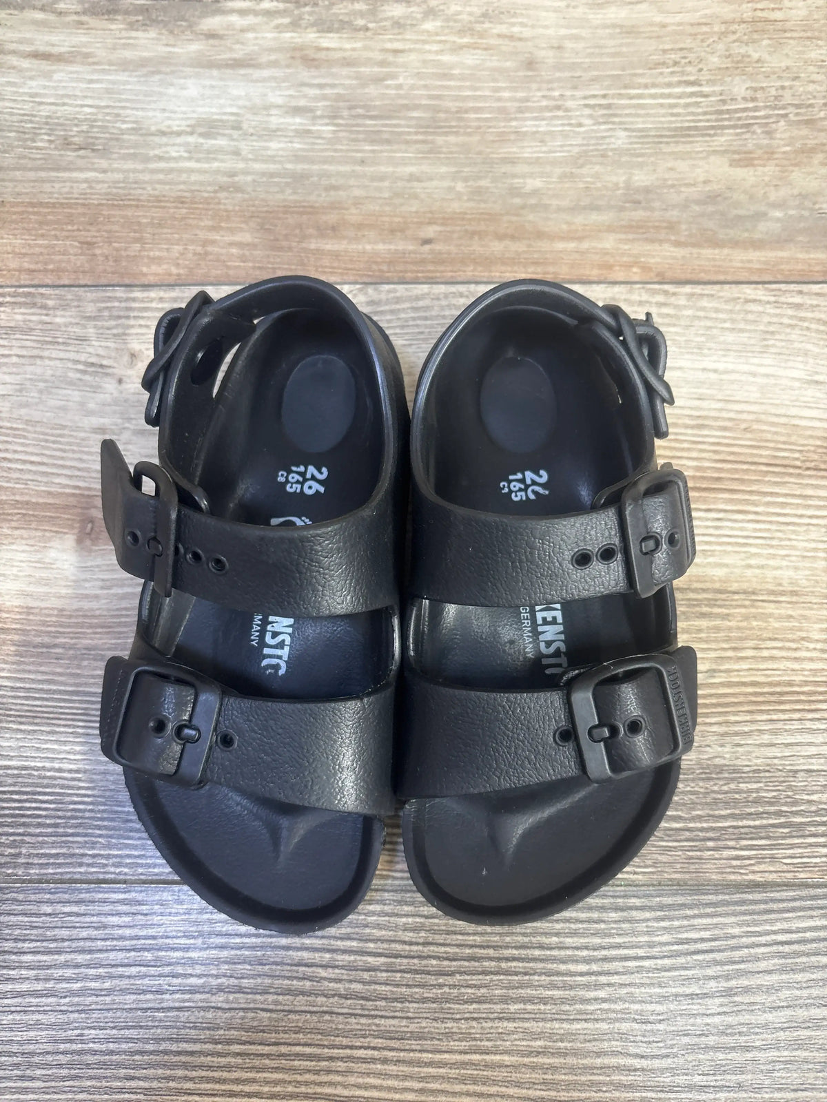 Top view of Birkenstock Milano EVA sandals showcasing three adjustable buckled straps and backstraps on a wood-grain surface