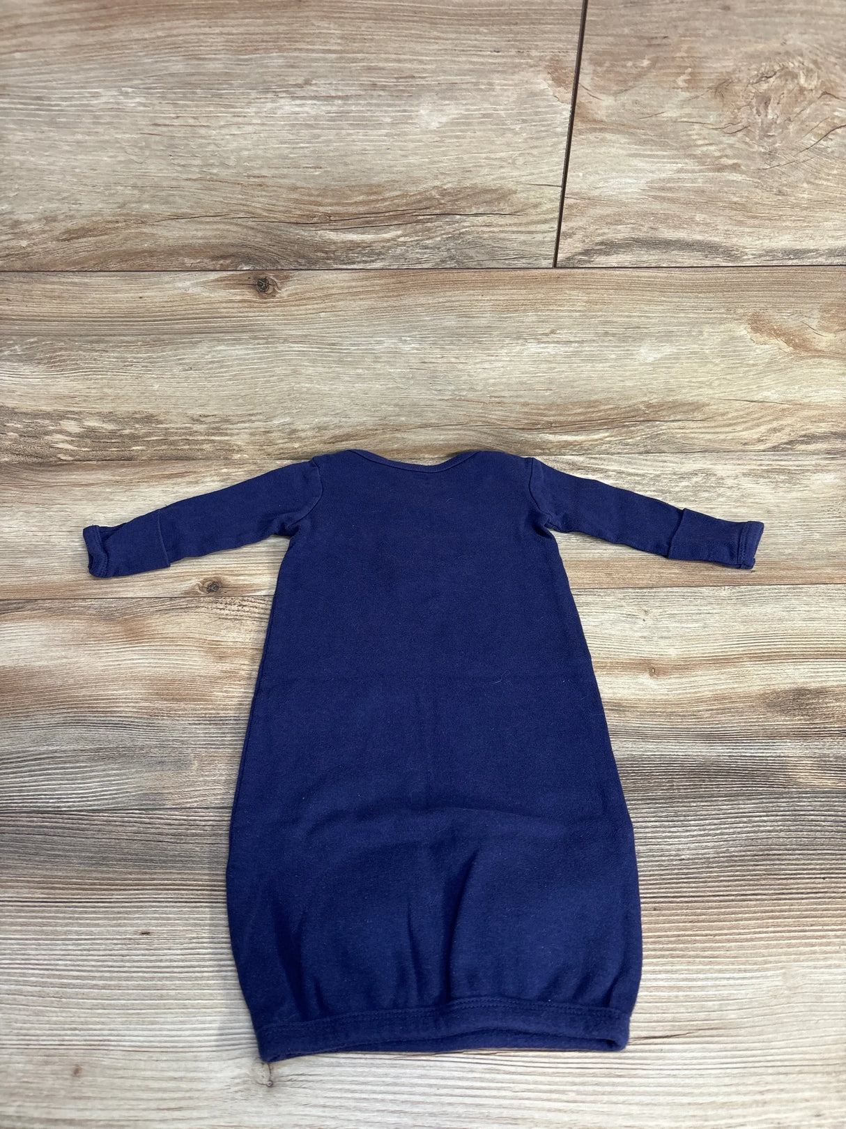 Navy blue long-sleeve infant gown laid flat on wood floor