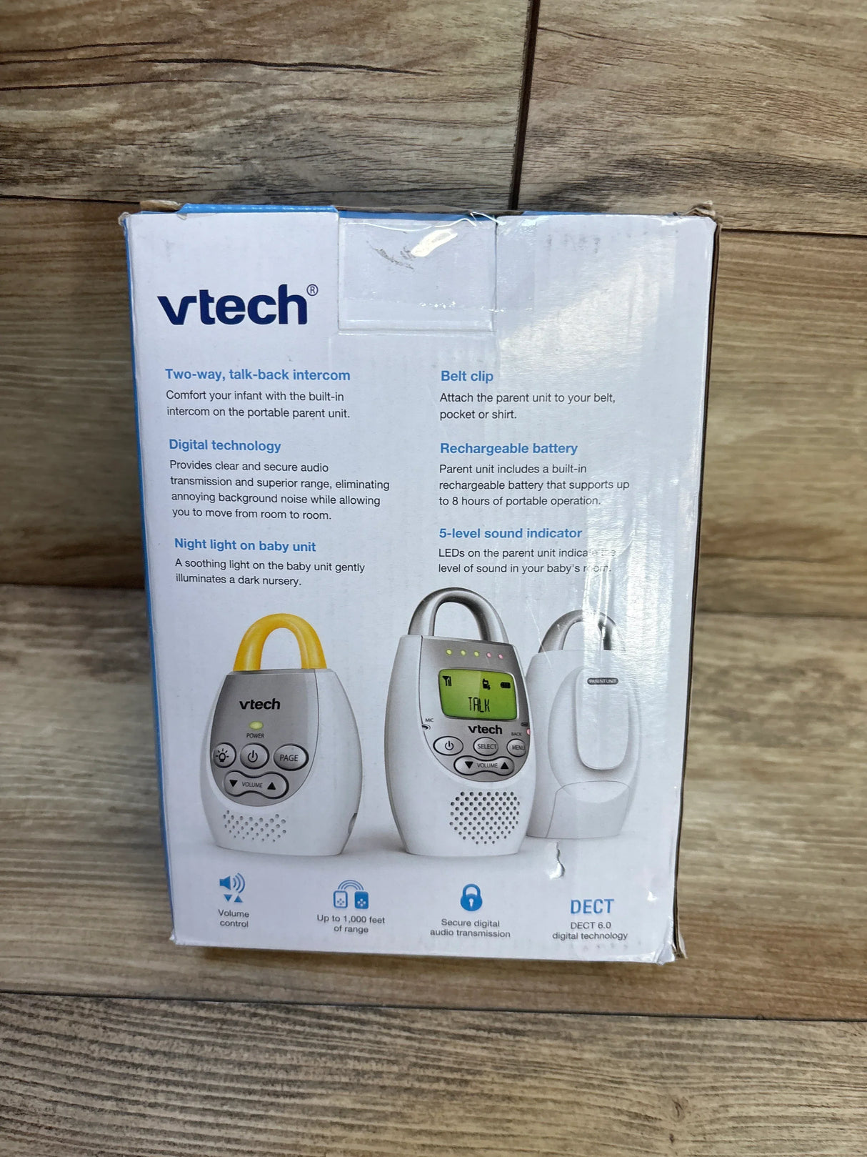 Front of VTech DM221-2 box showing two parent units, baby unit with belt clip and LCD display on wooden floor background