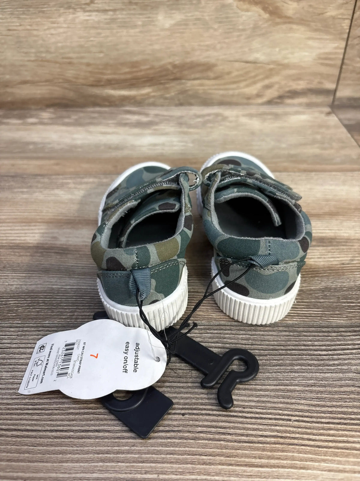 Rear view of green camouflage Wonder Nation sneakers showcasing double adjustable straps and white soles on wood flooring