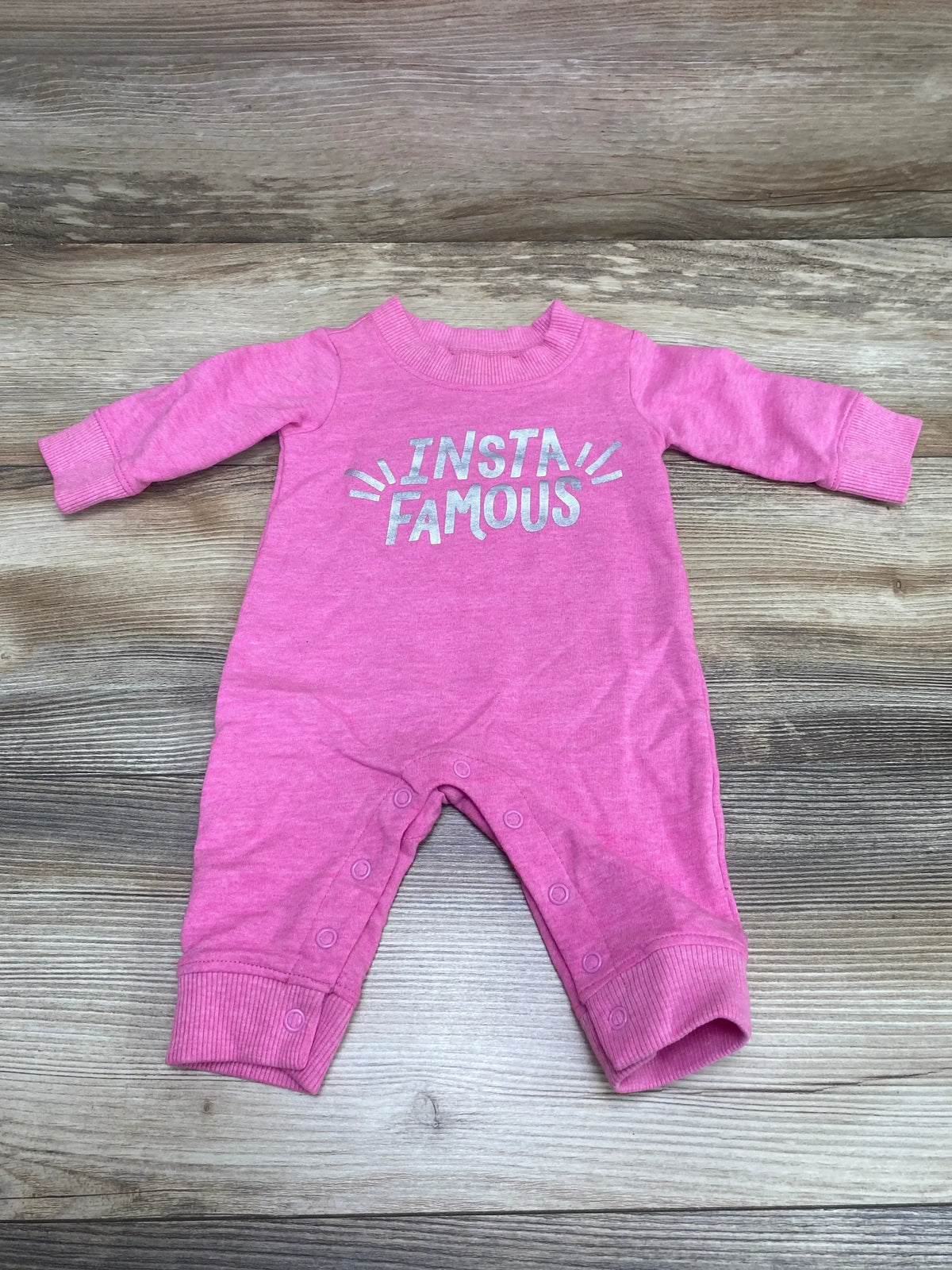 Flat lay of pink Carter’s coverall showcasing INSTA FAMOUS silver text and snap leg closures on light wood background