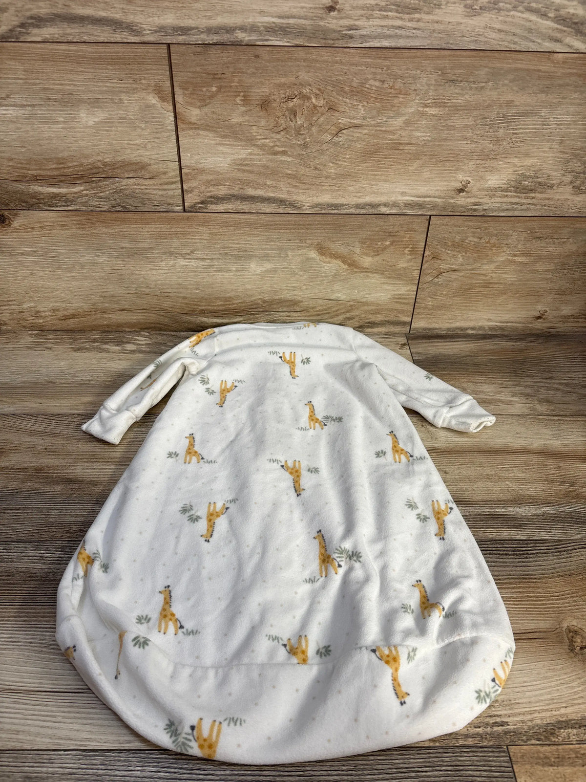 Flat lay of Carter’s white blanket sleep sack showcasing giraffe print and long sleeves on a wood floor
