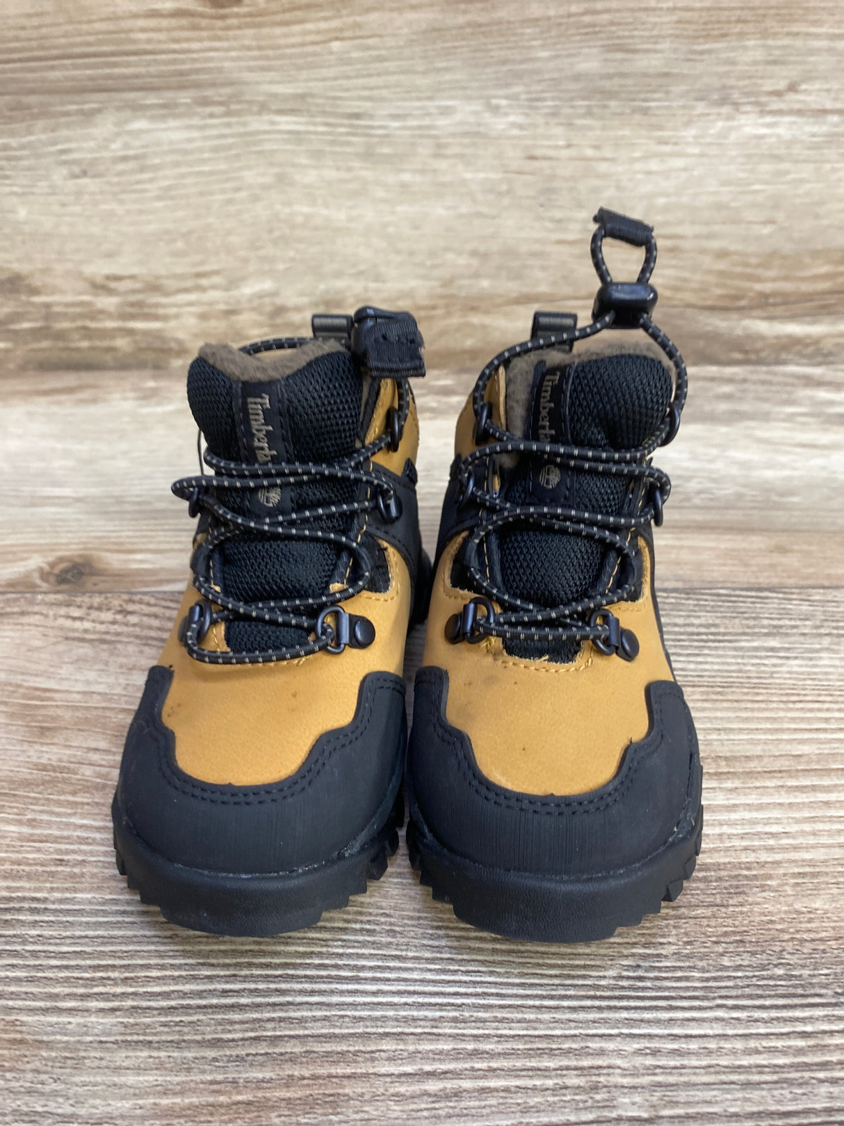 Pair of yellow and black Timberland hiking boots with laces on wooden floor