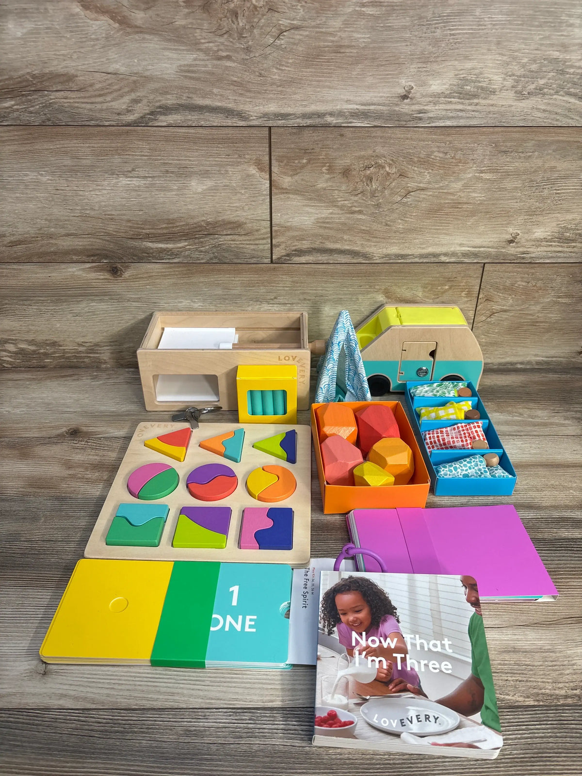 Top view of Lovevery The Free Spirit Play Kit showcasing toys, puzzles, stacking boulders, and play guide on wood floor